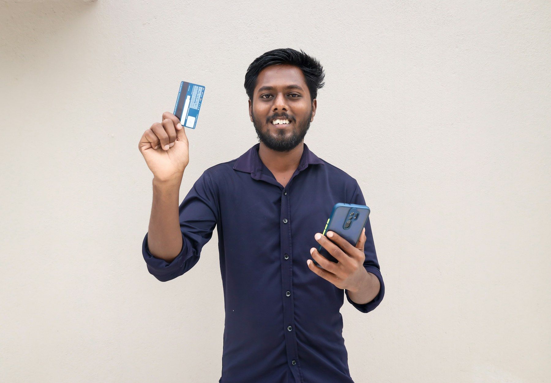 A smiling man holding a phone and a card, ready to pay
